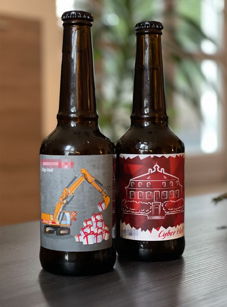 Bierflaschenetiketten, zwei Versionen für zwei unterschiedliche Sondereditionen als Kundengeschenk. Auf der einen version schaufelt ein Bagger einen Berg voller Weihnachtsgeschenke. Aus dem Führerhaus winkt ein Lebkuchenmännchen. Das andere Etikett zeigt ein stilisiertes Firmengebäude.